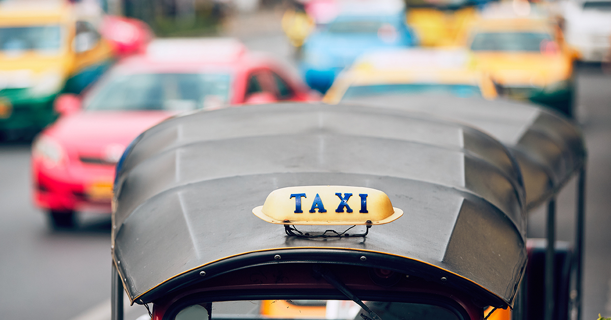 Taxi sign on the tuk tuk against traffic with colorful taxi cars. Busy street in Bangkok, Thailand